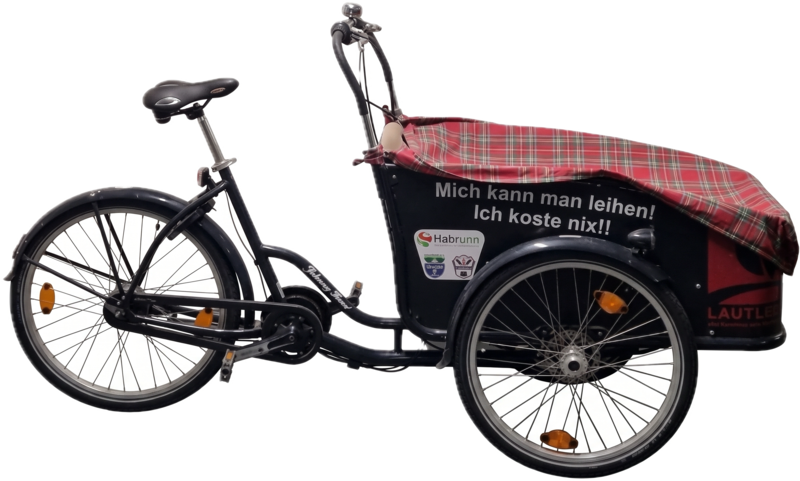 Das Lastenrad LAgenda: ein dreirädriges Lastenfahrrad mit schwarz-roter
              Transportbox und rot kariertem Regenverdeck. Auf der Box steht
              „Mich kann man leihen! Ich koste nix!!“